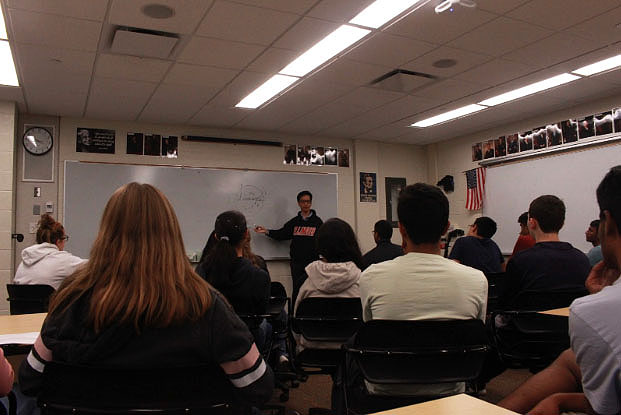 Chung continues his presentation of how hypnosis works. Students are gathered around the board and listen intently to his speech.