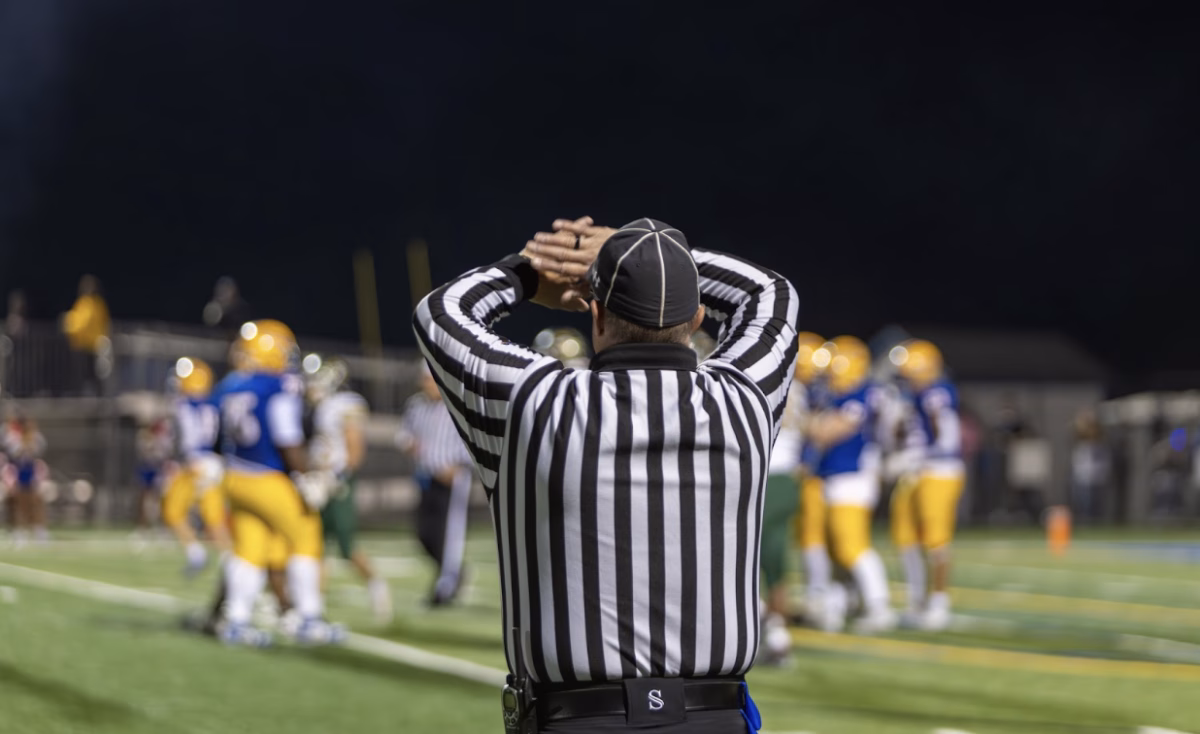 An official calls for the clock to stop during a football game. Teams are given three time-outs in one half, and officials are in charge of stopping the game for a team to meet on their side of the field.