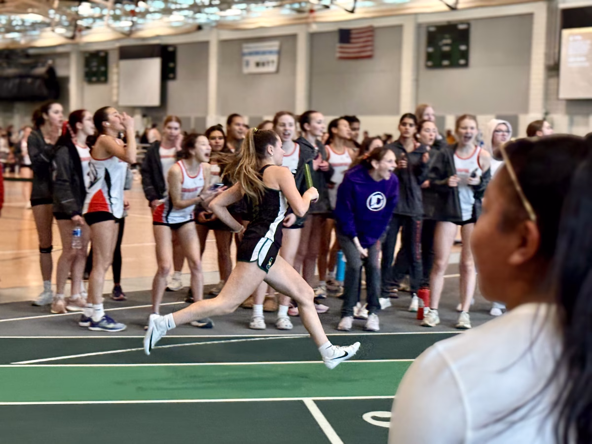 Trinity Robert ’28 runs in the 4x400 relay, with runners pushing through the final stretch of the race. Students crowd the sidelines, cheering as the event unfolds on the track.